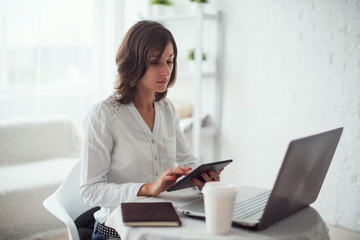 Freelancer using tablet pc, woman working on laptop computer at home