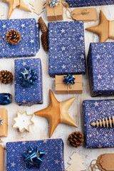 Creative chritmas composition. Presents in dark blue wrapping paper with silver stars and sparkles, wooden decorations, ornaments, paper tags on white table, overhead view, selective focus