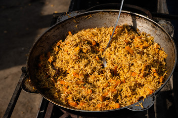 Tasty Uzbek pilaf in a cauldron on fire in the open air at street food festival