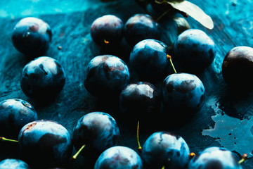 many fresh plums on blue background close up.