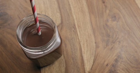 cocoa with red striped paper straw from glass jar on wood background with copy space shot from above
