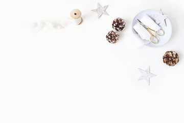 Christmas craft, winter wedding composition. Decorative corner Pine cones, silk ribbons, golden scissors on porcelain plate and wooden stars. White table background. Flat lay, top view