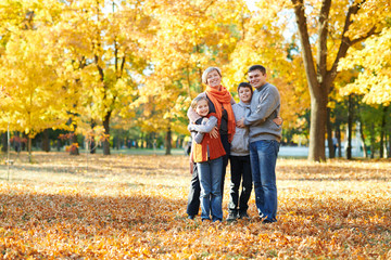 Fototapeta premium Happy family walks in autumn city park. Children and parents posing, smiling, playing and having fun. Bright yellow trees.