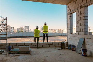 Two male builders at a construction site. Men looking into the distance to the panorama of the...