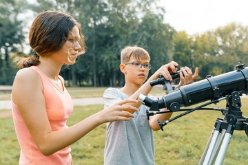 Children teenagers with telescope look at the sky in nature
