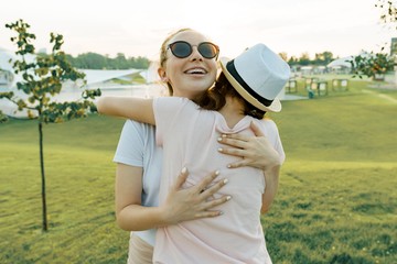 The friendship of two teenage girls, best girlfriends have fun in nature, on the green lawn of recreation park and entertainment. Embrace the greeting and parting.