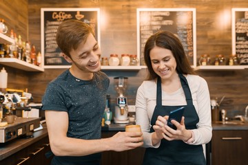 Couple of young male and female coffee shop owners near the counter, talking and smiling, coffee shop business concept