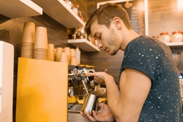 Young male barista makes a drink near the coffee machine. Coffee shop business concept