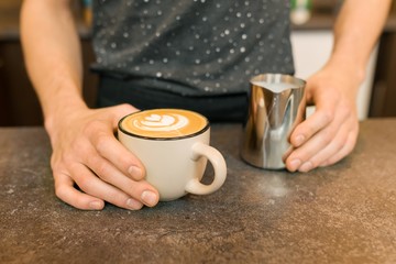 Closeup of latte art, hands of barista and iron mug with milk, background coffee house