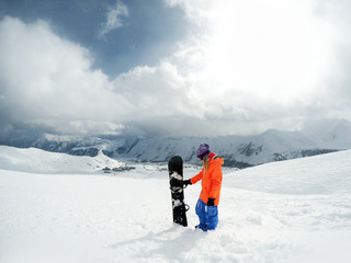 Female snowboarder standing with snowboard in her hand. Girl snowboarder posing with snowboard on background of mountain