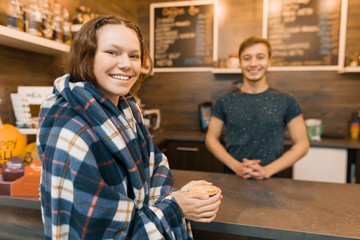 Autumn winter portrait of young teen girl with a cup of coffee and covered with woolen plaid blanket in coffee shop