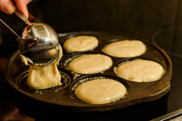 Spooning pancake dough into hot cast iron skillet.