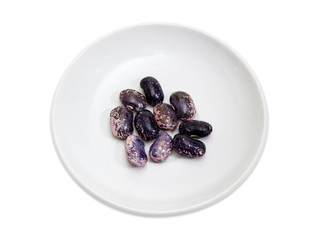 Purple speckled kidney beans on saucer on a white background