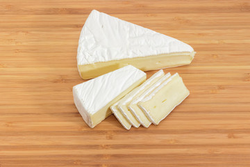 Partly sliced brie cheese on wooden cutting board