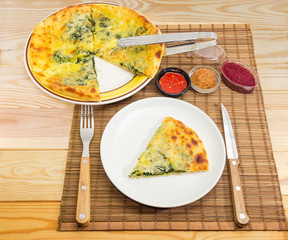 Partly sliced khachapuri on dishes, fork and knife, seasonings