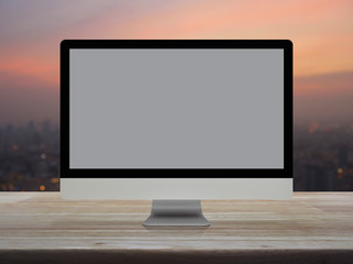 Fototapeta premium Desktop modern computer monitor with grey screen on wooden table over blur of cityscape on warm light sundown