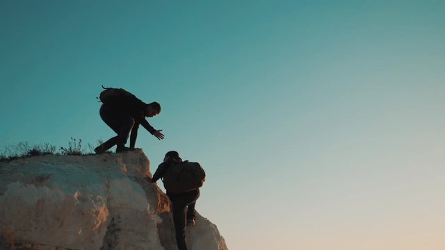 Teamwork friendship hiking help each other trust assistance silhouette in mountains. Backpacker helps to his friend to climb to rock. two travelers help stretching hand tourist concept adventure