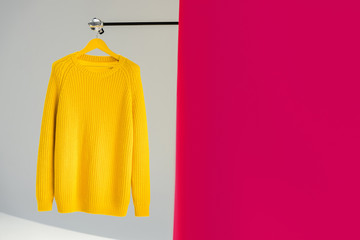 knitted yellow sweater on hanger on pink and grey background