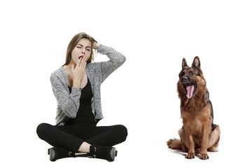 The yawning bored woman and her dog over white background. Shetland Sheepdog sitting in front of a...
