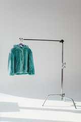 fluffy green faux fur coat hanging on rack at grey background