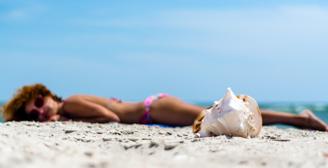 Fototapeta na wymiar large ocean shell on the sand against the background of a tanning girl in a colorful swimsuit on the beach