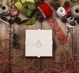 Naklejka na ściany i meble Closed plywood box with xmas tree on the cover on a wooden table surrounded by ribbons, cord, ropes and pine cones. Preparing for the new year.