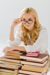 beautiful woman holding glasses near pile of books isolated on grey