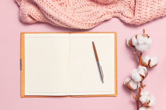 Female pink knitted sweater, cotton, open blank notebook, pen on pastel pink background top view flat lay. Lady winter Clothes. Cotton flowers. Lifestyle gentle female background