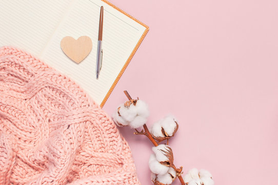 Female pink knitted sweater, cotton, open blank notebook, pen on pastel pink background top view flat lay. Lady winter Clothes. Cotton flowers. Lifestyle gentle female background