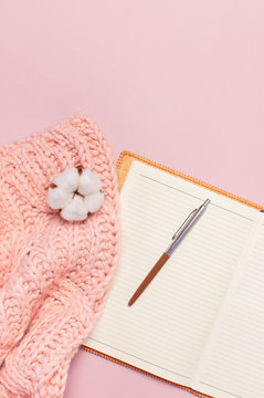 Female pink knitted sweater, cotton, open blank notebook, pen on pastel pink background top view flat lay. Lady winter Clothes. Cotton flowers. Lifestyle gentle female background