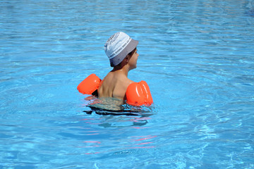 A boy 7 years old swiming and playing in a pool with resque rings