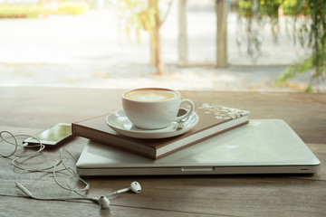 Cup of coffee on top of book and laptop on wooden table with cell phone.