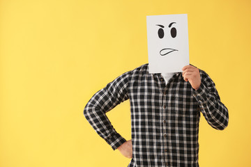 Man hiding face behind sheet of paper with drawn emoticon on color background