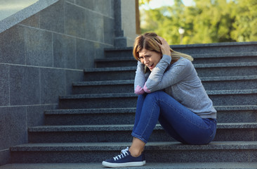 Woman having panic attack while sitting on steps outdoors - obrazy, fototapety, plakaty