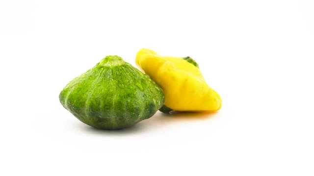 Two pattypan squashes - green and yellow. Rotating. Isolated on the white background. Close-up. Macro.