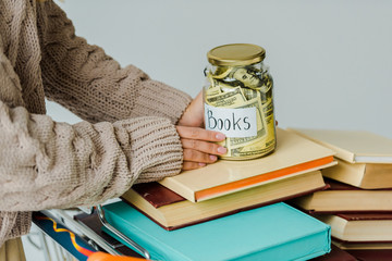 close up of female hands holding jar with cash on books