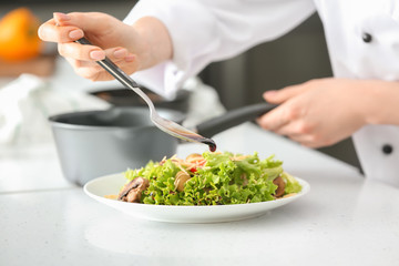 Young female chef dressing tasty salad in kitchen, closeup