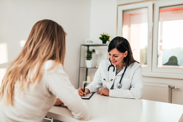 Fototapeta premium Beautiful female doctor filling out a form for her patient.