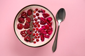 Yogurt with berries and cut dragon fruit in bowl on color background