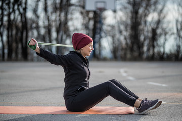 Young woman sitting on the playground and exercising with resistance band