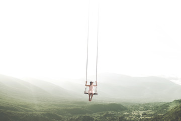 surreal moment of a woman having fun on a swing hanging from the sky