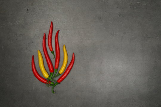 Top view on fire shape composed from hot chilli peppers layed down on grey kitchen table.