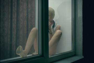 Woman in underwear sitting on a window sill at night. View from the outside.
