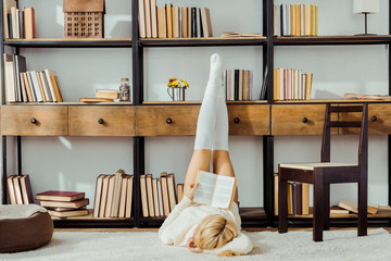 woman laying on carpet and reading book with legs on rack