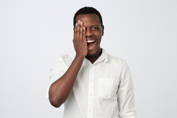 African young man in white shirt covering half face with hand