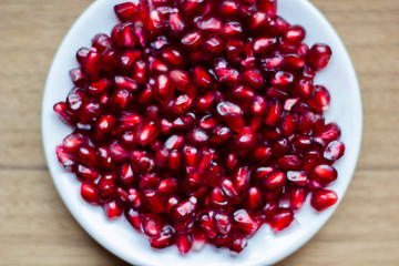 Pomegranate fruit (Latin: Punica granatum) is an exotic fruit with many vitamins and antioxidants. It is used within fruit juices and medicine. Top view of the fruit seeds on a white dish on the table