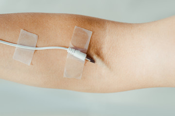 close up of female hand with attached white cable  like medical IV infusion isolated on grey, music concept