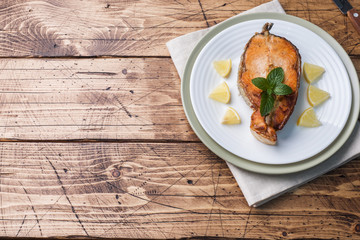 Steak baked fish salmon on a plate with lemon. Wooden table.