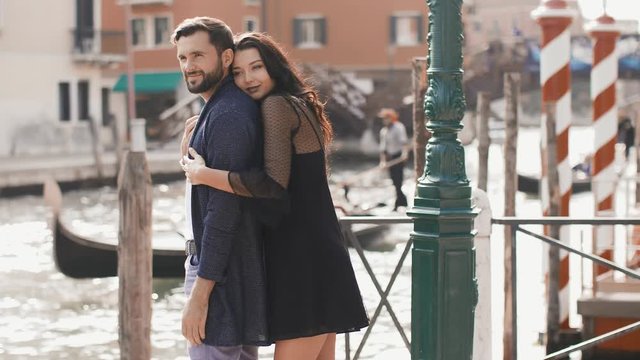 Love - romantic couple in Venice on pier. Young couple on travel vacation holidays hugging kissing and embracing near canal with gondolas boats on summer sunny day, Venice, Italy. Beautiful woman