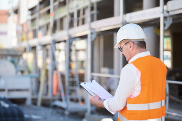 Architekt, Mann, Bauleiter auf der Baustelle mit klemmbrett und Plan von hinten